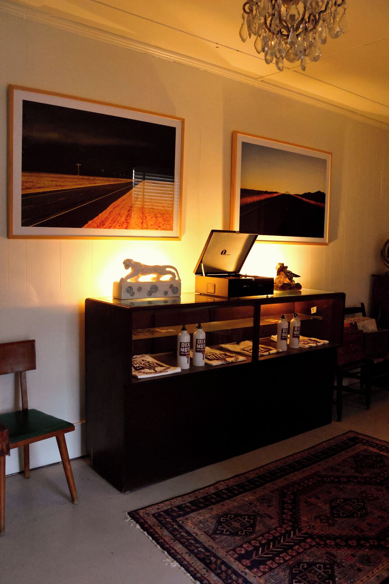 A living room with a dark wooden cabinet, two framed landscape paintings, a laptop, and a chandelier.