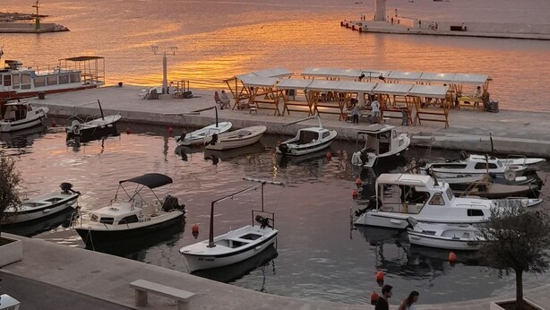 Een jachthaven met afgemeerde boten, een voetpad en een zonsondergang op de achtergrond.