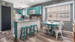 Una cucina moderna con mobili color petrolio, un'isola centrale con sgabelli e un'area pranzo con tavolo e sedie rotonde.