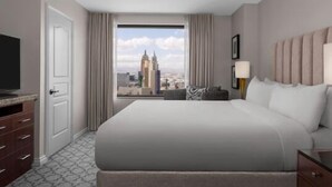 A hotel room with a large bed, a television, a desk, and a view of a cityscape.
