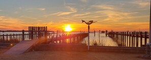 Un atardecer sobre el frente marítimo con un muelle de madera y una estatua.