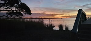 Vista lacustre con atardecer, agua tranquila y un muelle.