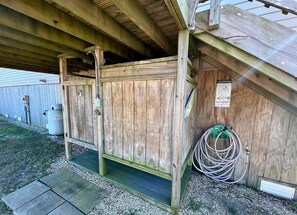 Una estructura de madera con techo de metal, un calentador de agua y una manguera enrollada contra la pared.