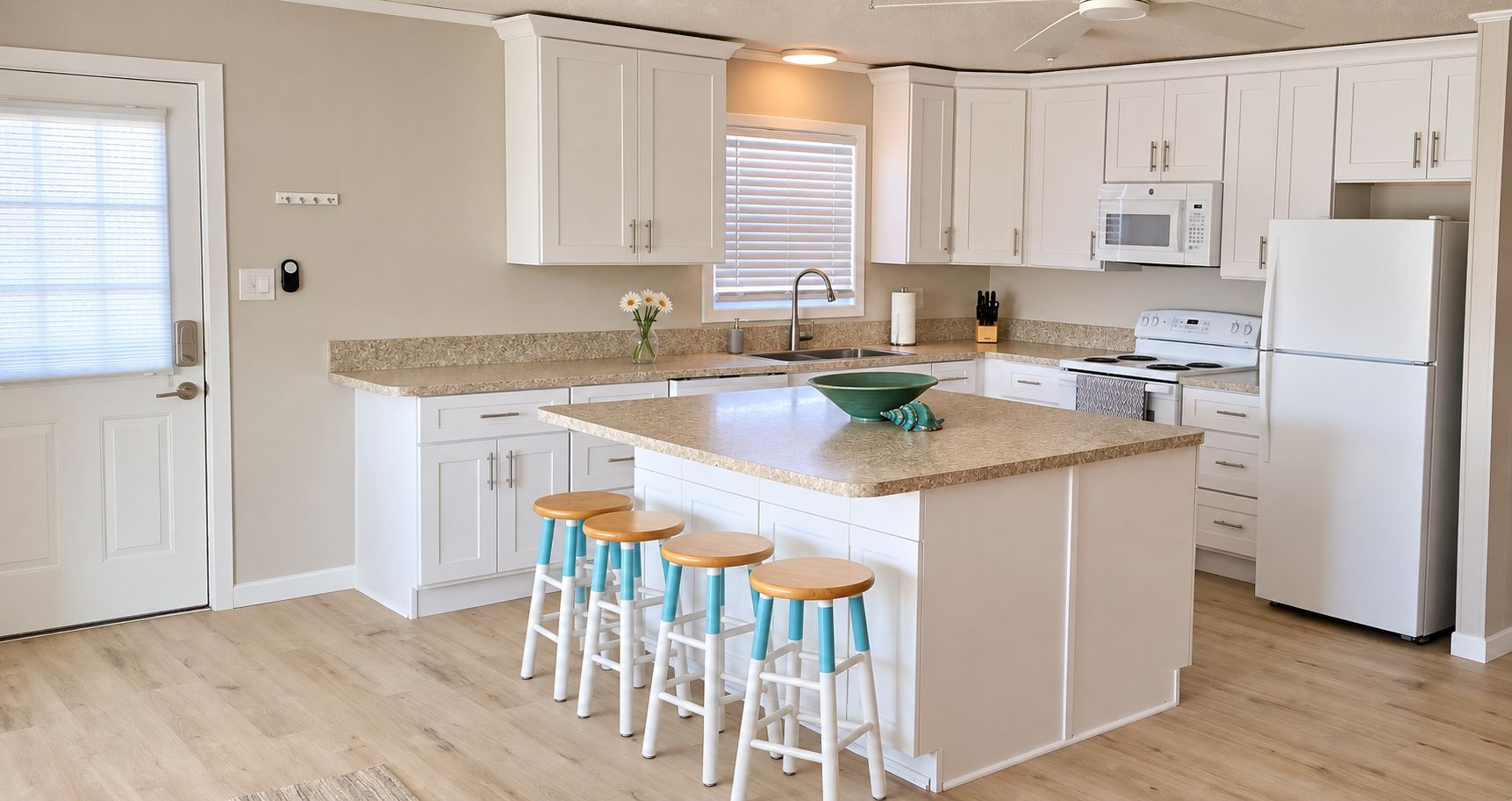 A kitchen with white cabinets, a central island with stools, a microwave, and a refrigerator.