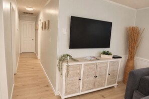 A hallway with a white door, a mounted TV, a white console with plants, and a wicker vase.