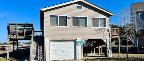 A two-story house with a garage, a small deck, and a covered area with a sign that reads "EAT. SLEEP. BEACH."