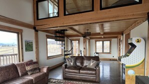 Un salon spacieux avec un canapé en cuir marron, un tapis à motifs et un plafond en bois.