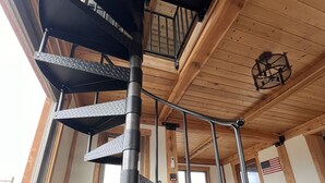 Un escalier en colimaçon avec des rampes en métal et des marches en tôle à losanges, menant à un étage supérieur en bois.