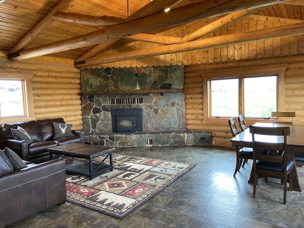 A log cabin interior with a stone fireplace, leather furniture, and a large window.