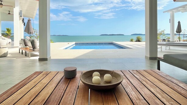 Une table en bois avec un bol et un objet décoratif, une piscine et une vue sur la mer et les îles.