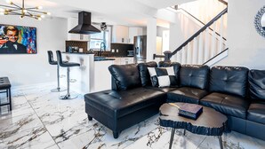 A modern living room with a sectional sofa, a coffee table, and a bar area with stools. - Gatsby Theme Near Downtown w Game Room, EV Charger (Lake Geneva)