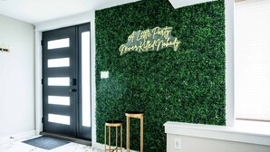 A modern entrance with a black door, a green wall with a text sign, and two gold stools. - Gatsby Theme Near Downtown w Game Room, EV Charger (Lake Geneva)
