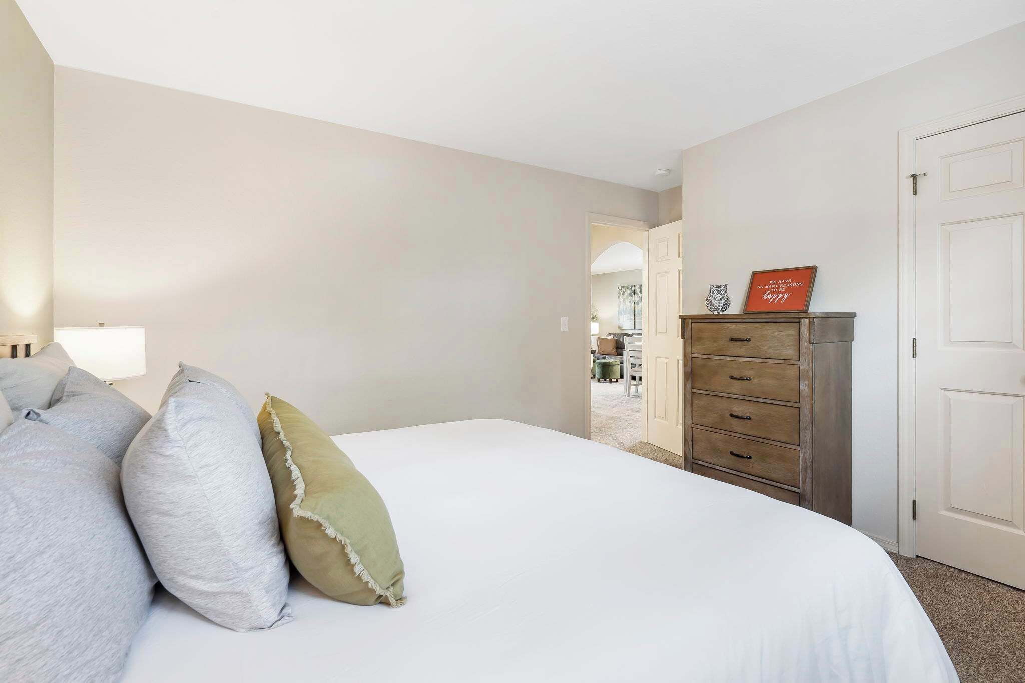 A bedroom with a bed, pillows, a dresser, and a door.