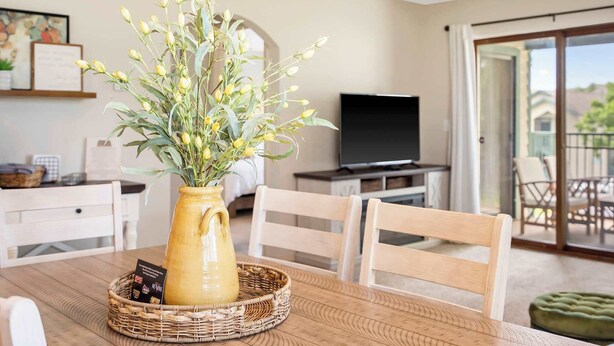 Un coin repas avec une table en bois, un vase rempli de fleurs et un téléviseur en arrière-plan.