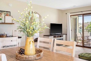 A dining area with a wooden table, a vase with flowers, and a television in the background. - Branson Cozy Bungalow in Premier Location! (Branson)