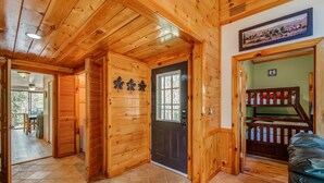 A wooden interior with a black door, a bench, and a framed picture on the wall. - Blueridge Bunk House Wrap-around Deck! (Blue Ridge)