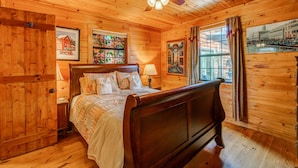 A wooden-paneled room with a bed, a ceiling fan, and framed pictures on the walls. - Blueridge Bunk House Wrap-around Deck! (Blue Ridge)