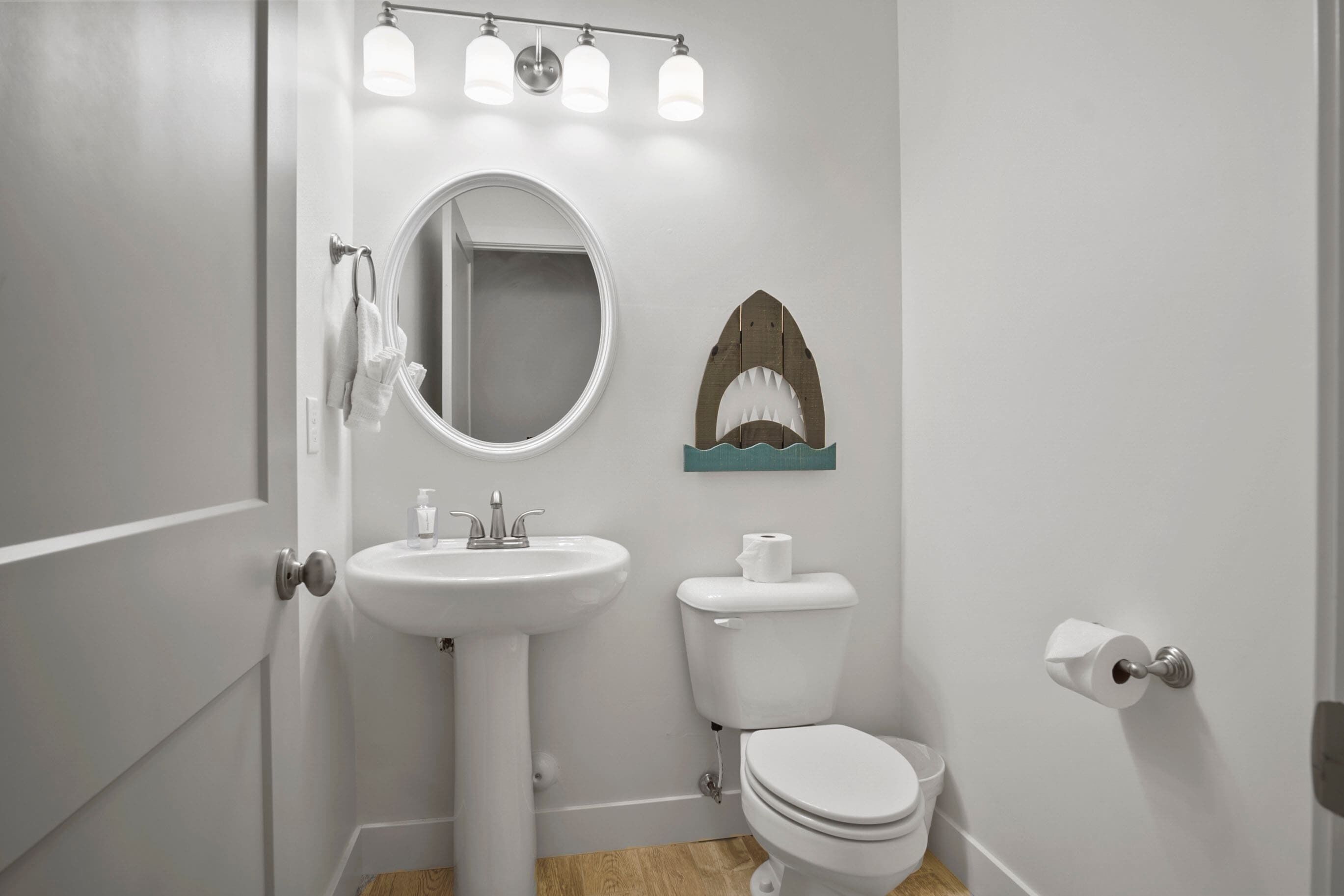 Een badkamer met een witte wastafel, ronde spiegel en een haai-decoratie aan de muur.