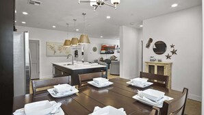 A dining area with a wooden table set for four, a kitchen in the background, and a decorative wall with a world map and artwork. - By the Sea Ocean Vibes in the Mountains! (Washington)