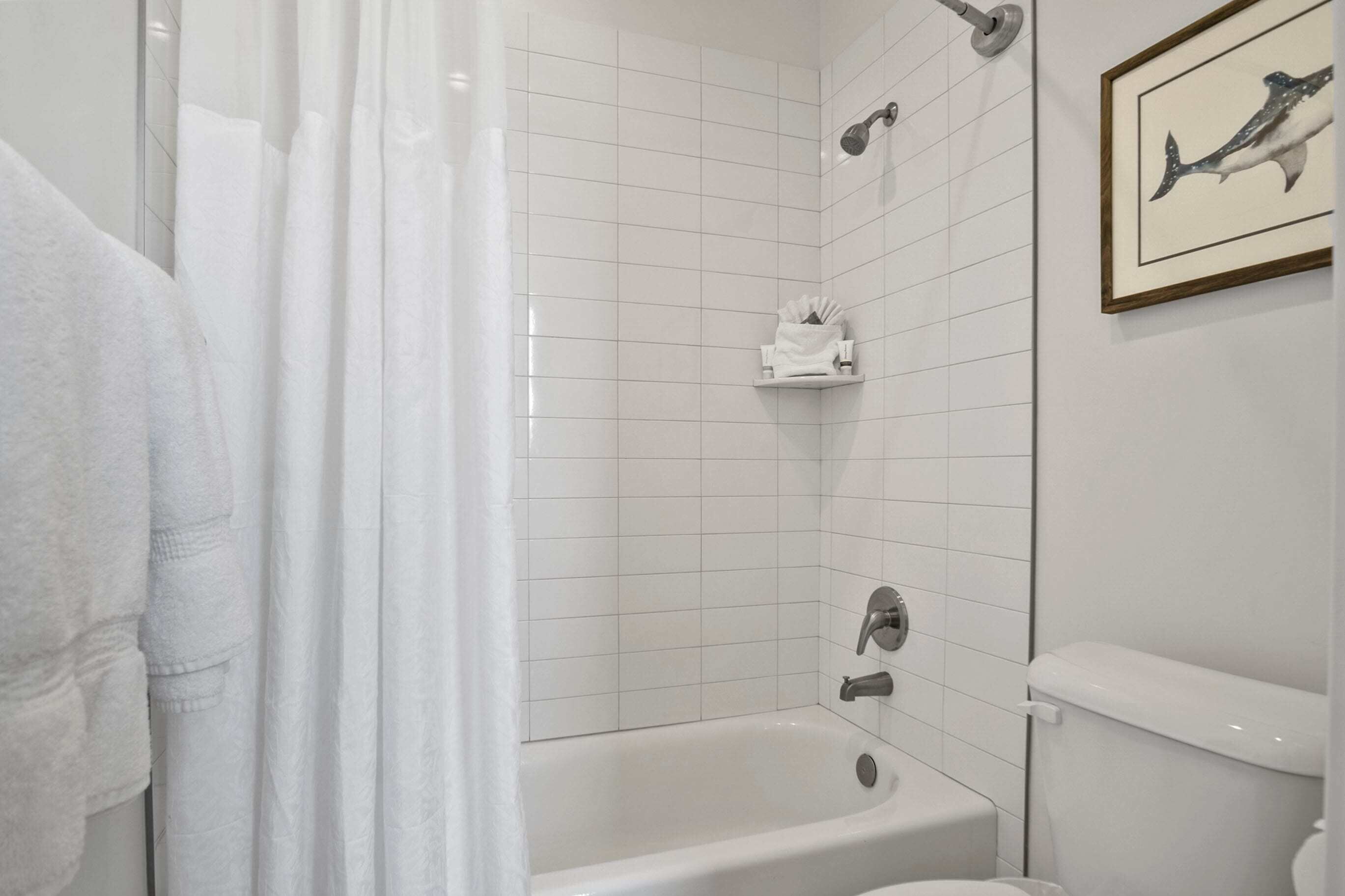 A bathroom with a bathtub, a shower, and a toilet. There is a towel rack and a framed picture on the wall.