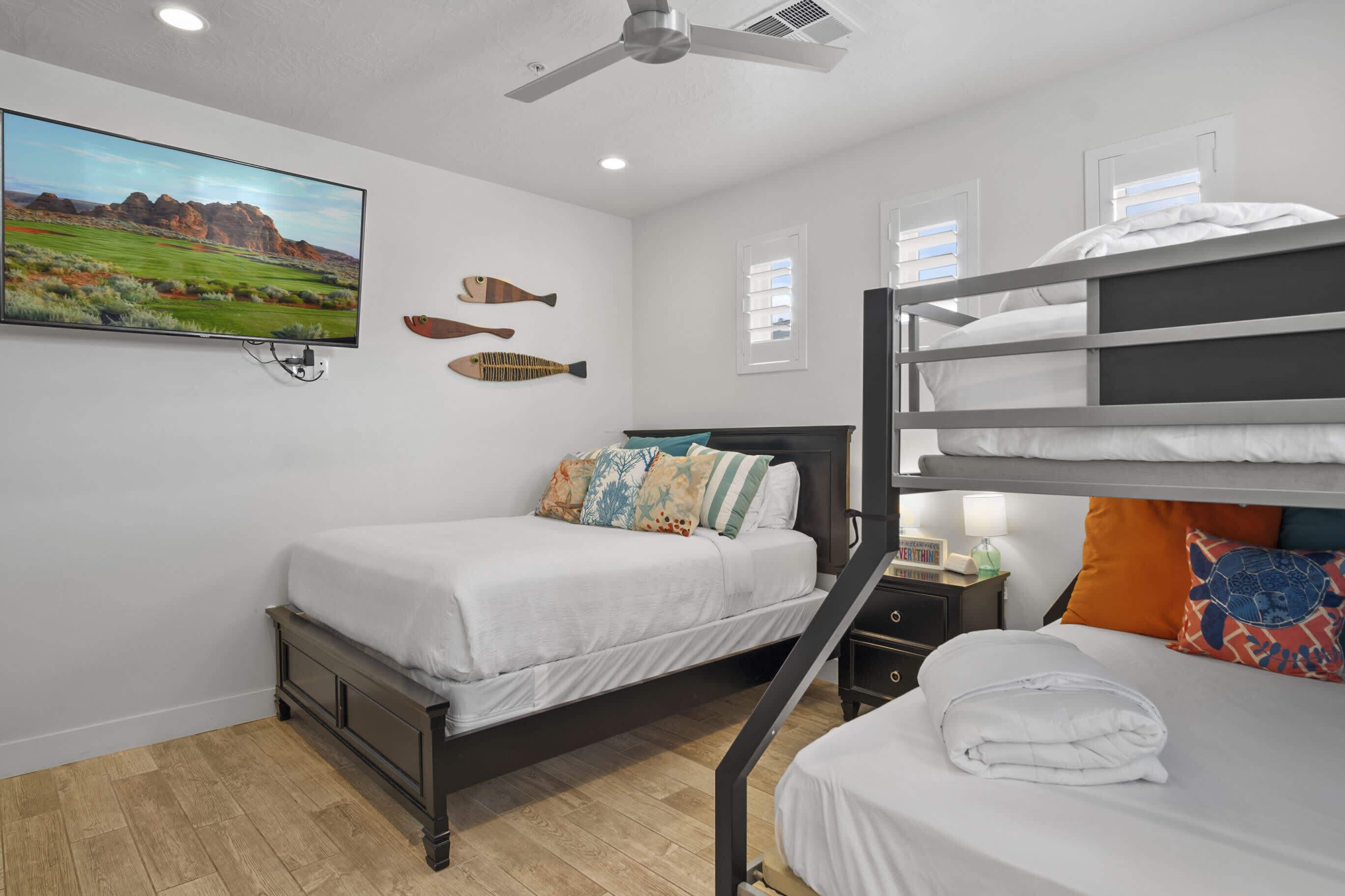 A hotel room with two beds, a TV, ceiling fan, and decorative fish on the wall.
