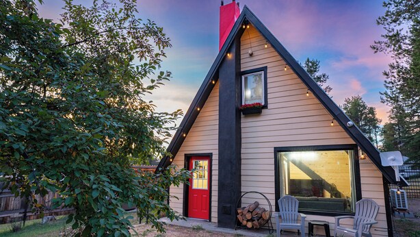 Una cabaña acogedora con puerta roja, ventanas grandes y chimenea.
