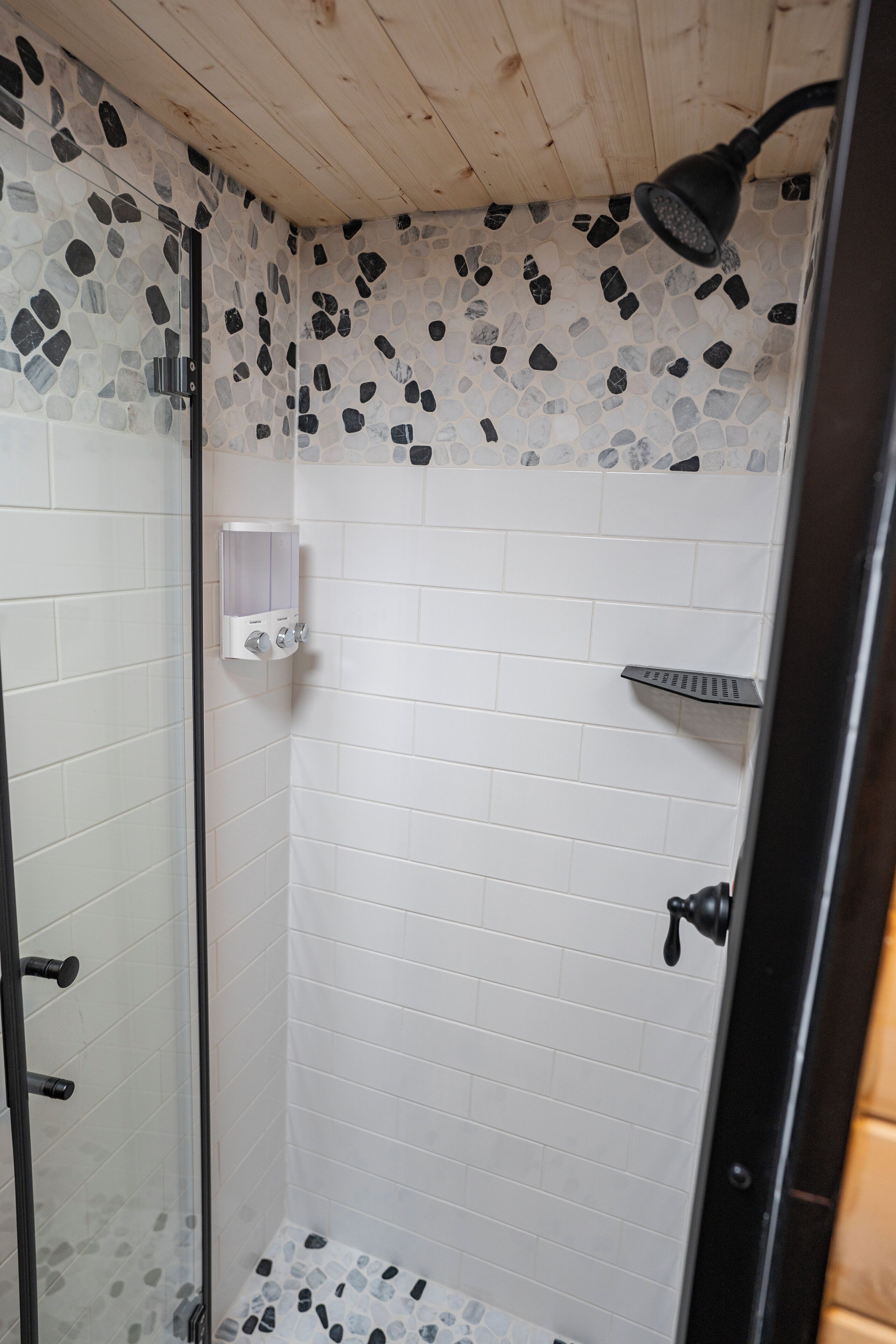 A shower with mosaic tiles, a glass door, and a wooden ceiling.