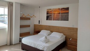 Un dormitorio moderno con cabecera de madera, cama con ropa blanca, mesita de noche, cómoda de madera, armario con estantes de madera y un ventanal con cortinas.