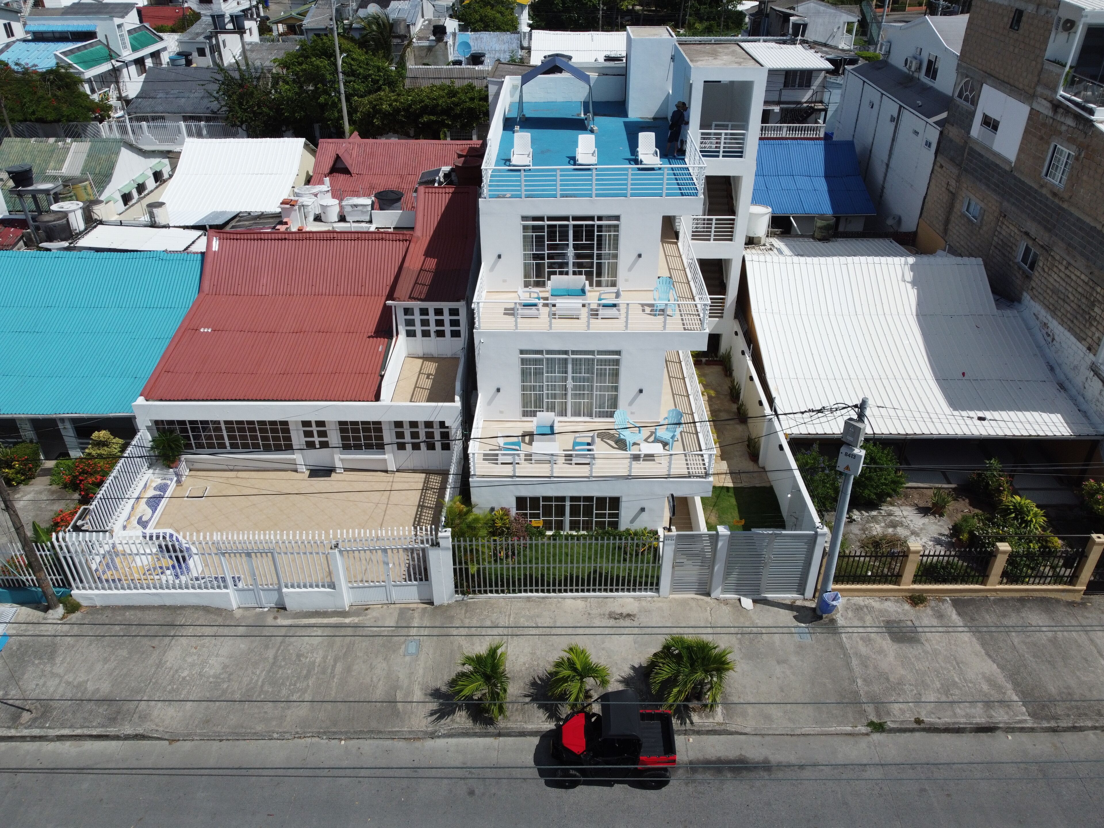 A multi-story building with a rooftop pool, a fenced parking area, and a street view with a parked vehicle.