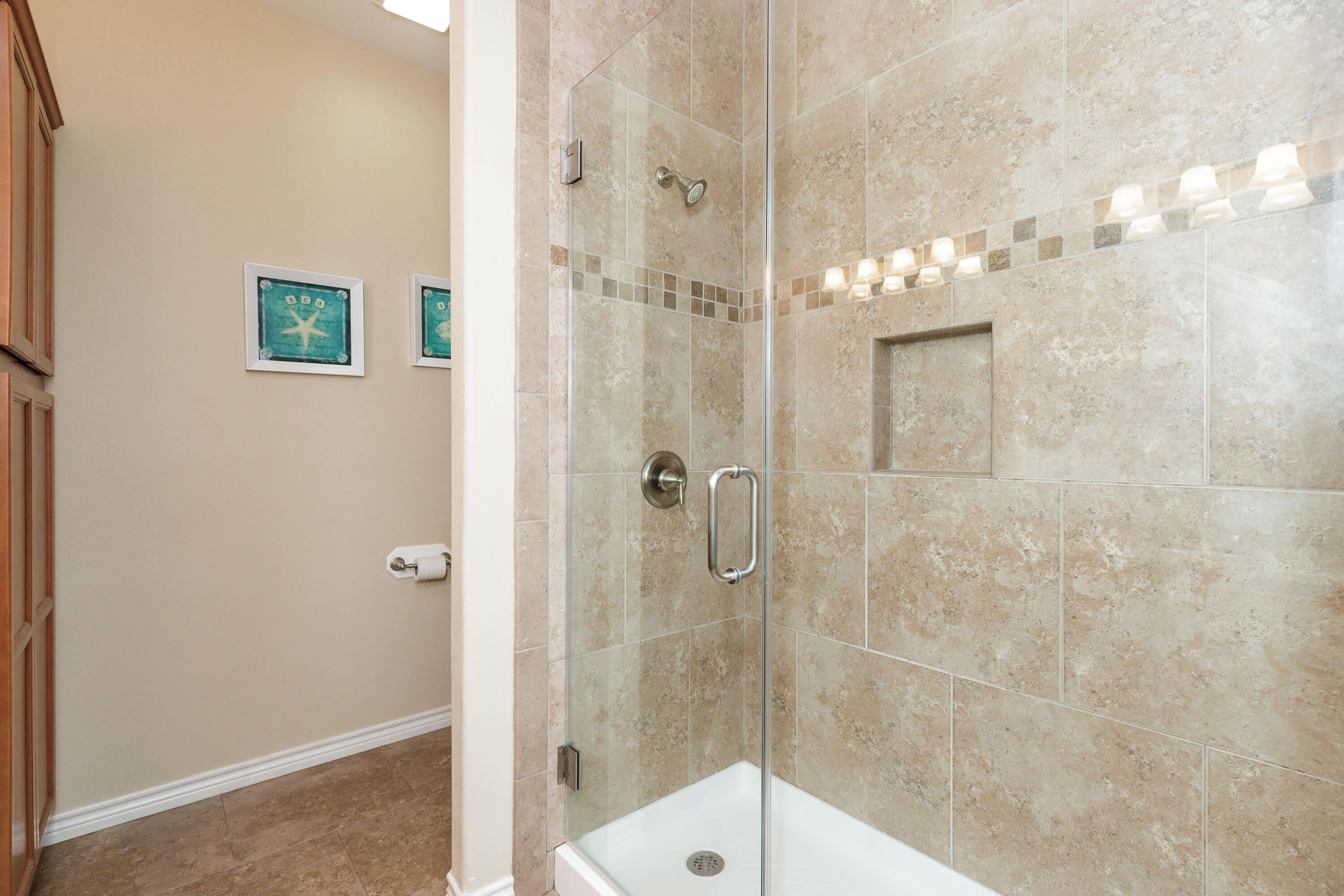 A shower area with a glass door, beige tiles, and a small square tile accent.