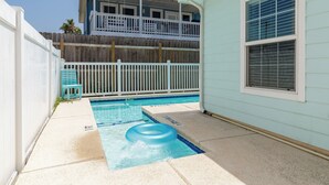 A backyard with a swimming pool, a white fence, and a two-story building with a balcony. - Comfy 2 bedroom | Pets & Shared Pool (Port Aransas)