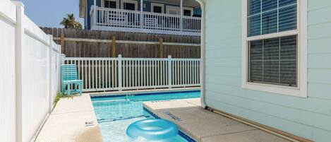 A backyard with a swimming pool, a white fence, and a two-story building with a balcony.