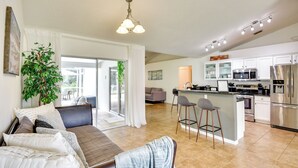 A modern kitchen with stainless steel appliances, a dining area with a sofa and bar stools, and a large window with curtains. - Beach Gear & Fire Pit: Palm Coast Group Escape (Palm Coast)