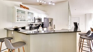 A modern kitchen with white cabinets, stainless steel appliances, and a granite island with bar stools. - Beach Gear & Fire Pit: Palm Coast Group Escape (Palm Coast)
