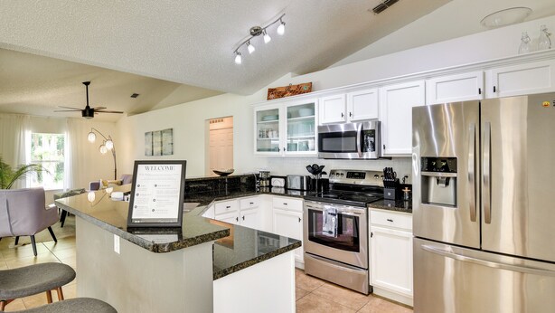 A modern kitchen with white cabinets, stainless steel appliances, a granite countertop, and a bar area with stools. - Beach Gear & Fire Pit: Palm Coast Group Escape (Palm Coast)