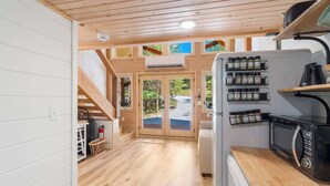 A kitchen with wooden floors, a microwave, and a coffee maker. There is a window with a view of greenery. - Cedar Creek - Glamping in the Ozarks! (Walnut Shade)