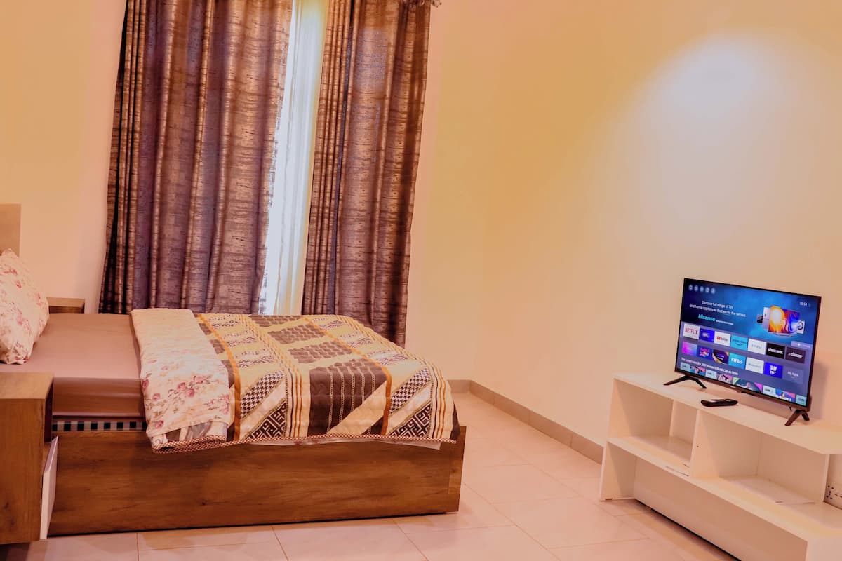 Une chambre à coucher avec un lit en bois, un téléviseur posé sur un meuble et des rideaux.