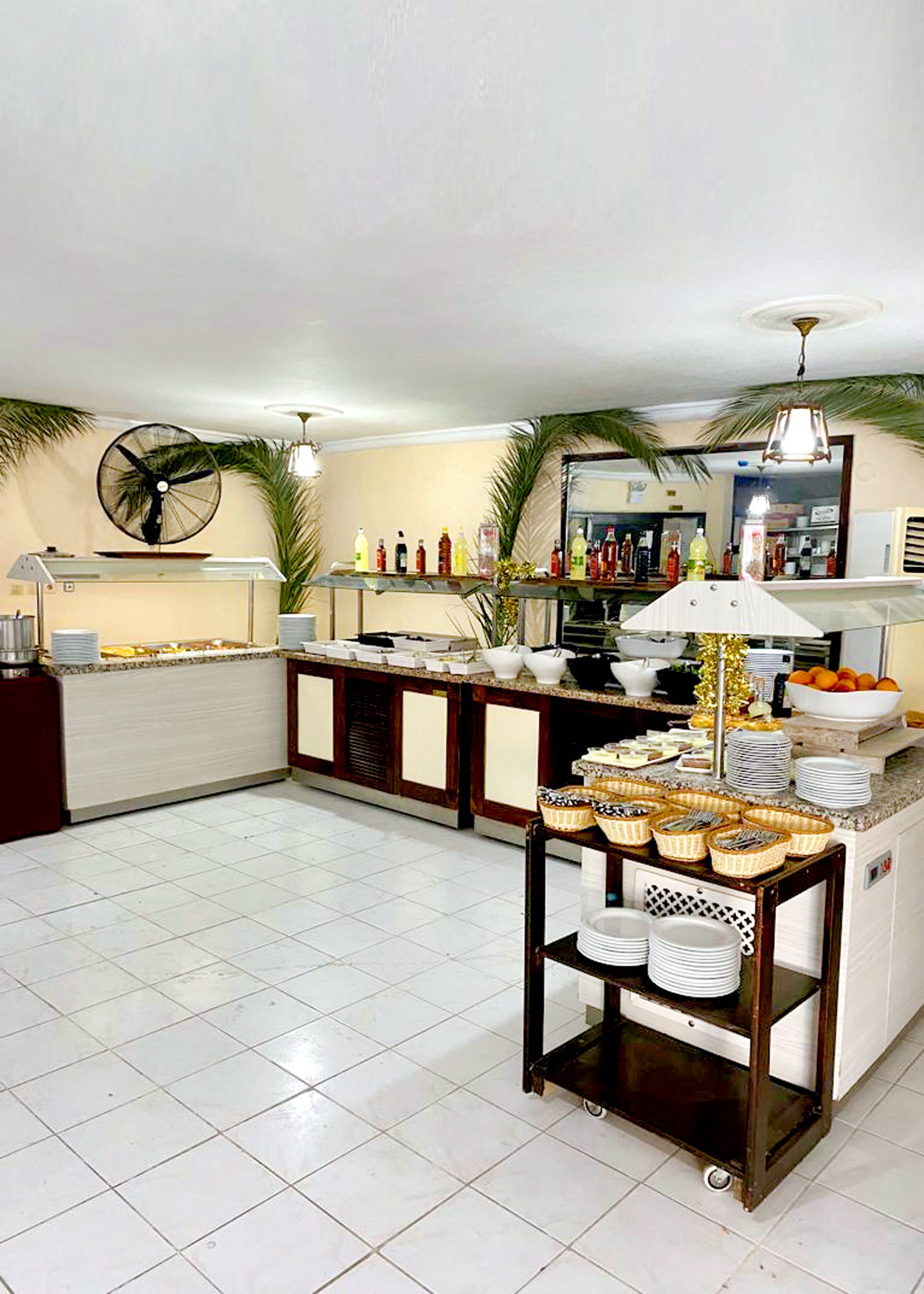 A spacious kitchen with a central island, white tiled floor, and a variety of food items and utensils on the counter.