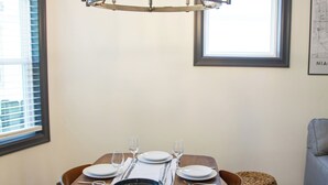 Ein Essbereich mit einem Holztisch, gedeckt für vier Personen, einer Chandelüster und Blick durch ein Fenster.