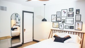 Ein Schlafzimmer mit einem Bett, einem Deckenventilator, einem Nachttisch, einem Spiegel und einer Wand mit gerahmten Bildern.