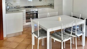 A modern kitchen with white cabinetry, a dining table with chairs, and a tiled floor.