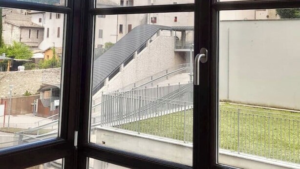 A view through a window with a metal railing, overlooking a building with a tall tower and a staircase leading to a lower level.
