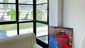 A room with a large window, a white sofa, and a colorful painting on the wall.