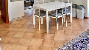 A modern kitchen with white cabinets, a dining table with chairs, and a patterned rug.