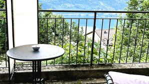 A balcony with a table and a cushion, overlooking a mountainous landscape. - Close to Franklin College and Lugano (Collina d'Oro)