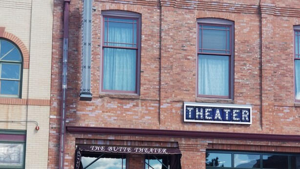 Een bakstenen theater met een etalage waarop 'THEATER' staat en een bord boven de ingang met de tekst 'THE BUTTE THEATER'.