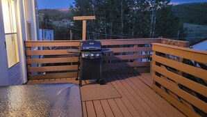 Een houten terras met een barbecue en een houten bank.