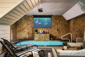 Un espace piscine intérieure comprenant des chaises longues, un écran de projection et un jacuzzi.