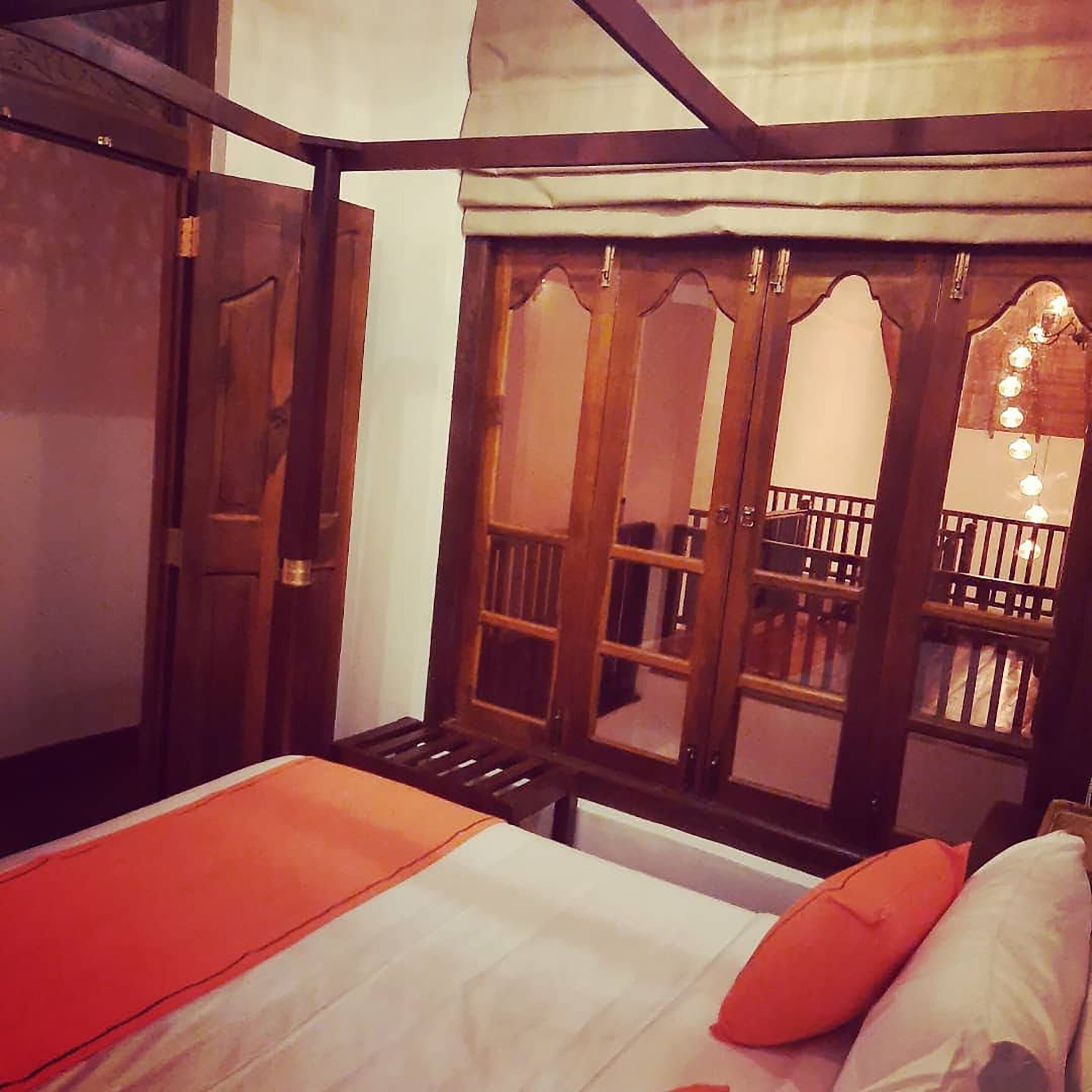 A room with a bed, wooden doors, and a balcony with lights.