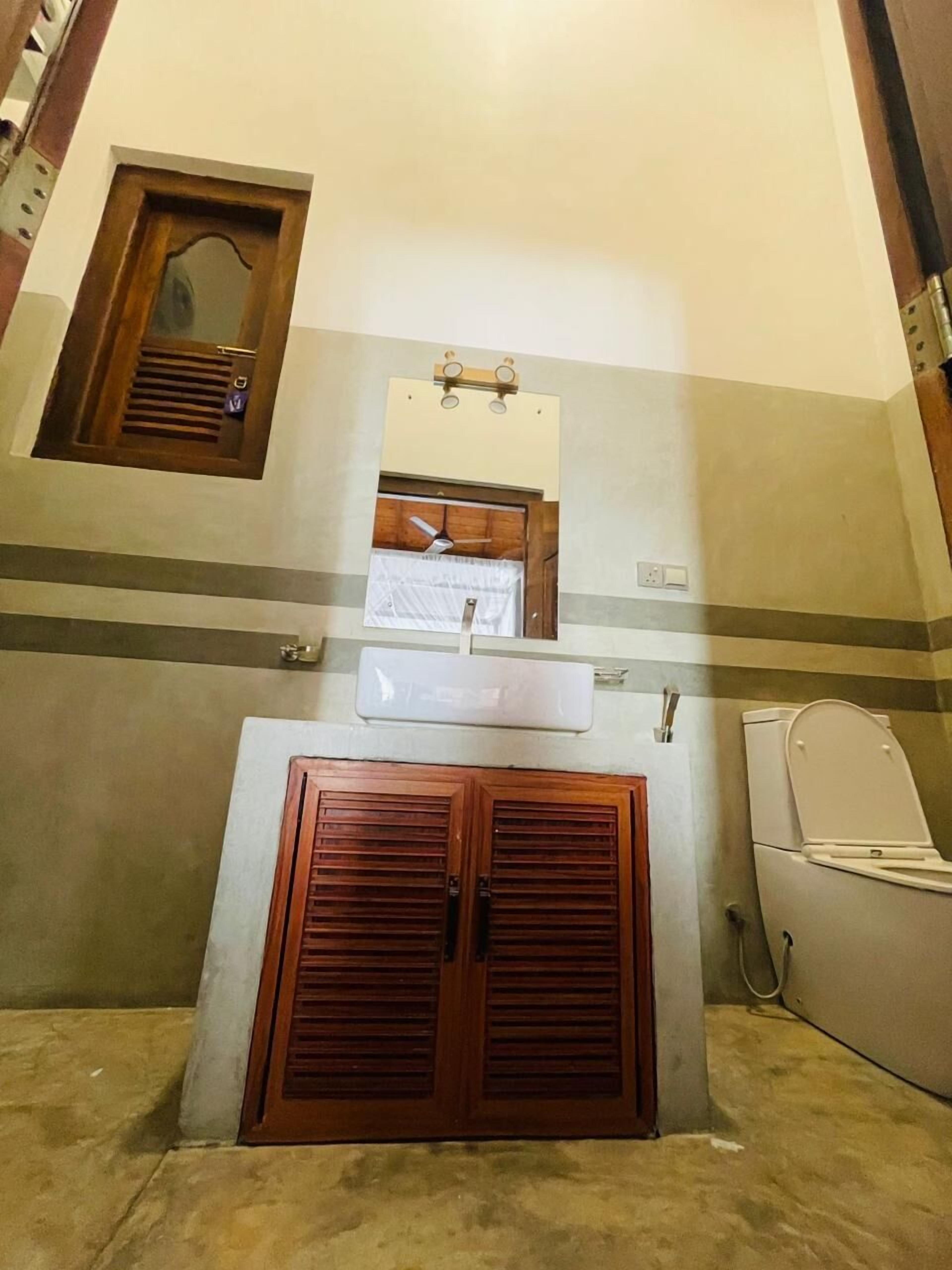 Un baño con puerta de madera, un lavabo blanco, un espejo y un ventilador de techo.